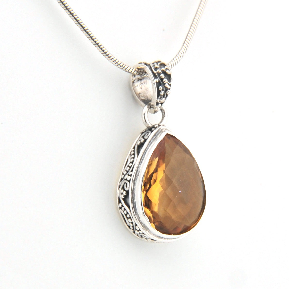 Teardrop-shaped citrine pendant on a silver chain against a white background
