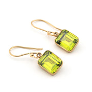 Gold earrings with green square stones on a white background