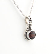 Silver necklace with a circular pendant featuring a red gemstone on a white background