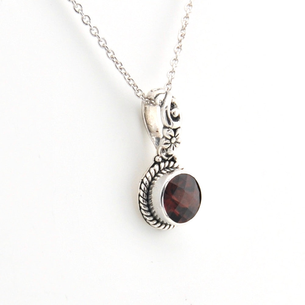 Silver necklace with a circular pendant featuring a red gemstone on a white background