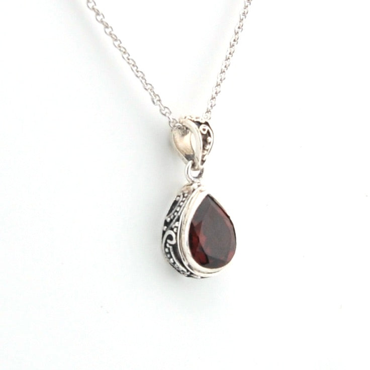 Silver necklace with a teardrop-shaped garnet pendant on a white background