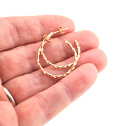 Gold hoop earrings held in a hand against a white background