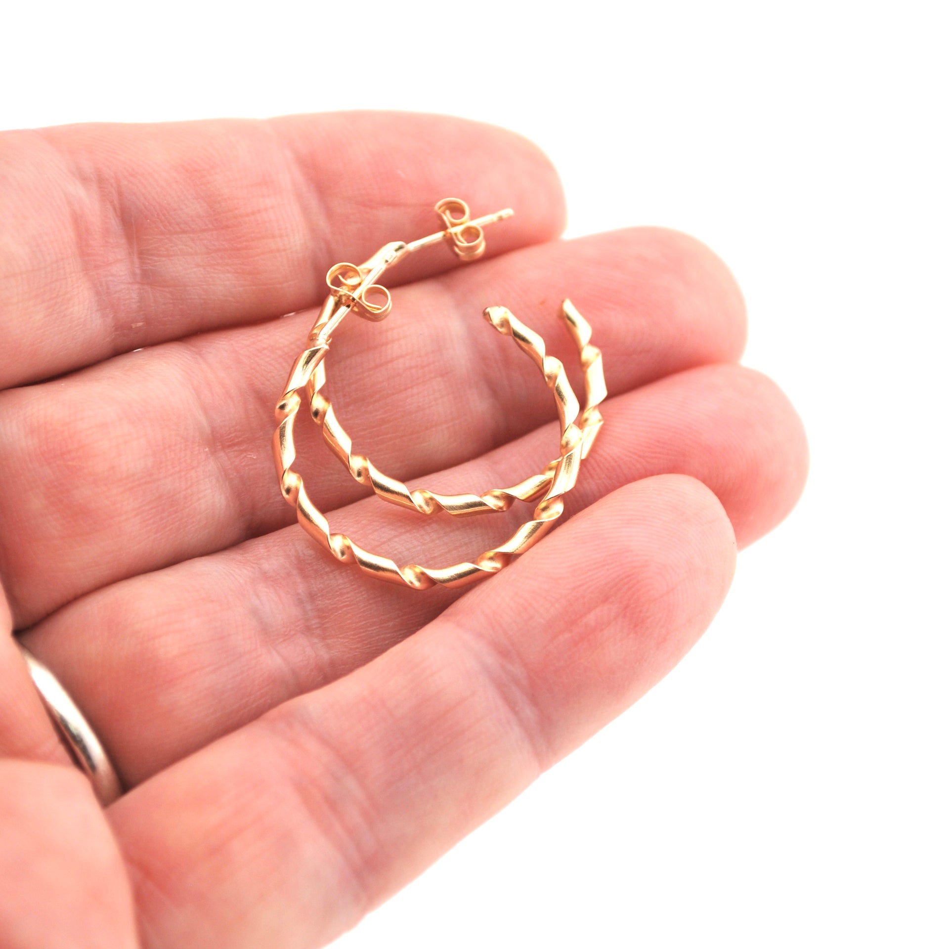 Gold hoop earrings held in a hand against a white background