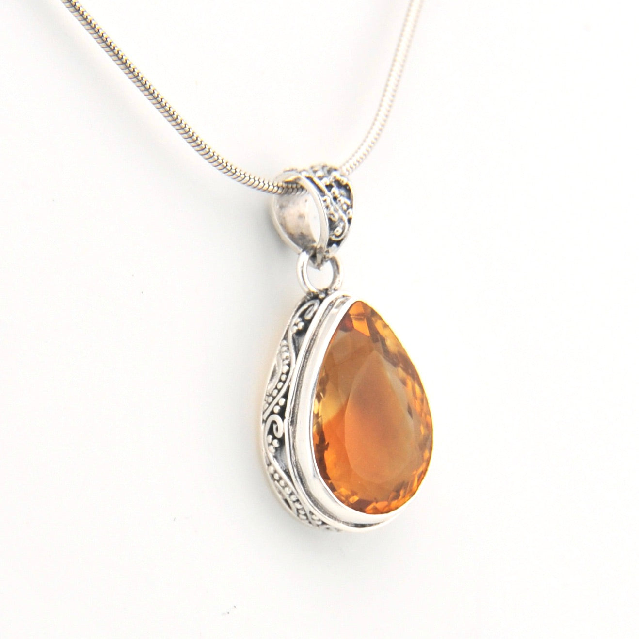 Silver pendant with a teardrop-shaped orange gemstone on a white background