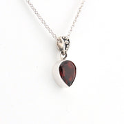 Silver necklace with a teardrop-shaped red gemstone pendant on a white background
