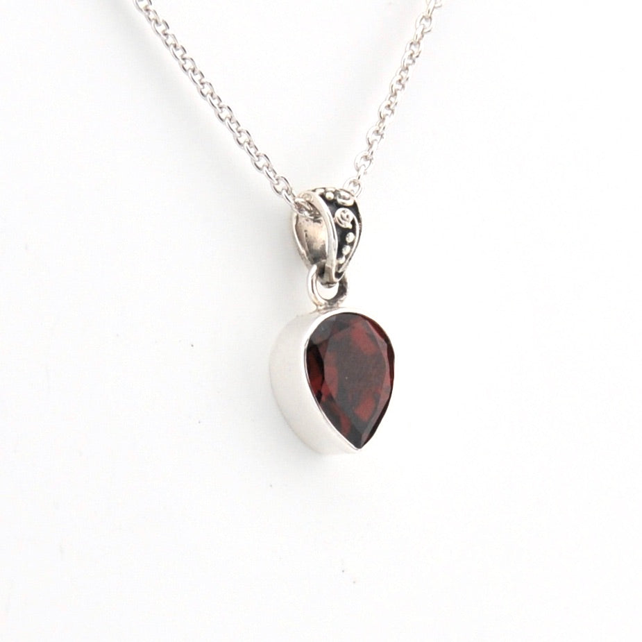 Silver necklace with a teardrop-shaped red gemstone pendant on a white background