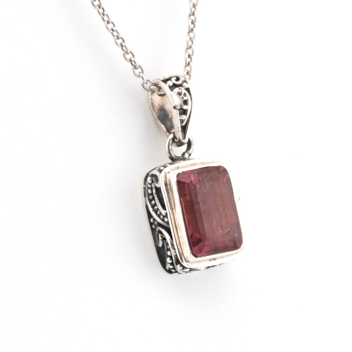 Silver pendant with a red gemstone on a white background