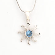 Silver sun-shaped pendant with a blue gemstone on a white background