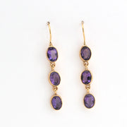 Gold earrings with purple gemstones on a white background