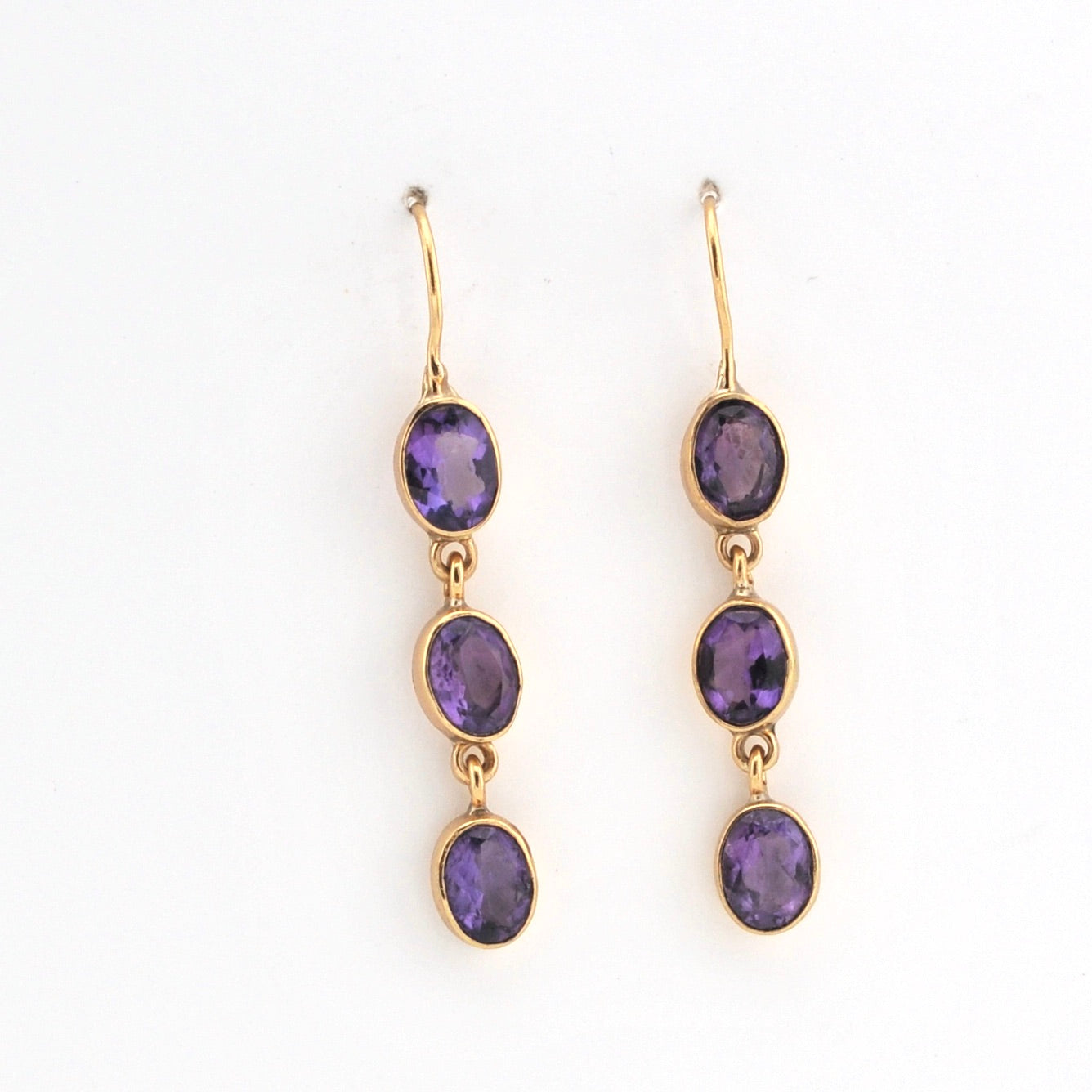 Gold earrings with purple gemstones on a white background
