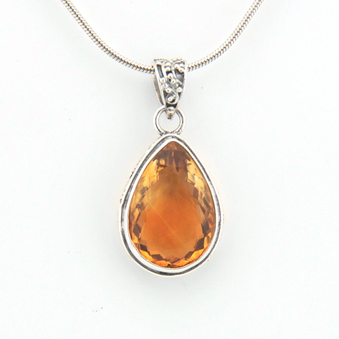 Teardrop-shaped citrine pendant on a silver chain against a white background