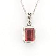 Silver pendant with a red gemstone on a white background