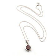 Silver necklace with a pendant featuring a red stone on a white background