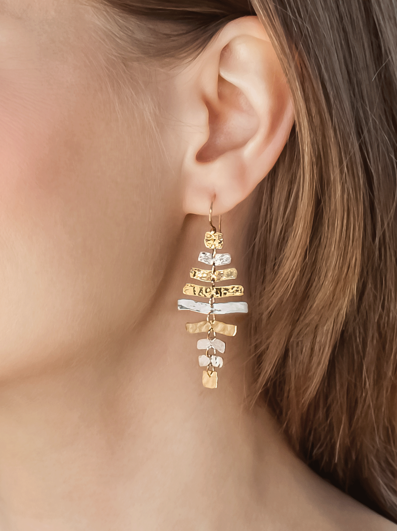 Gold and silver earring worn by a person with blurred background