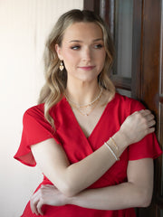 Woman in a red dress with jewelry standing indoors.