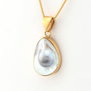 Gold pendant with a large teardrop-shaped pearl on a white background