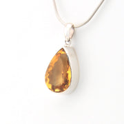 Teardrop-shaped citrine pendant on a silver chain against a white background
