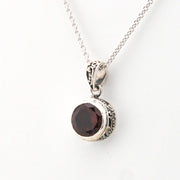 Silver necklace with a round red gemstone pendant on a white background