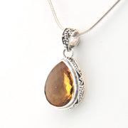 Teardrop-shaped citrine pendant on a silver chain against a white background