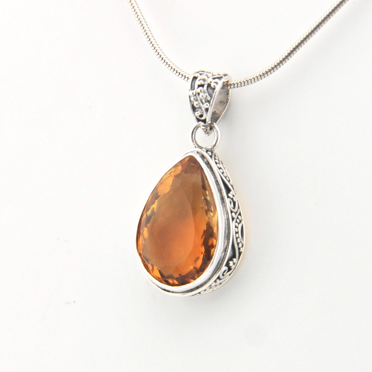 Teardrop-shaped citrine pendant on a silver chain against a white background