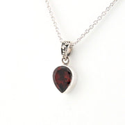 Silver necklace with a teardrop-shaped garnet pendant on a white background