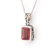 Silver pendant with a red gemstone on a white background