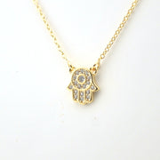 Gold necklace with a Hamsa hand pendant on a white background