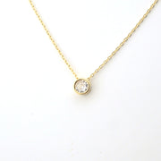 Gold necklace with a round diamond pendant on a white background