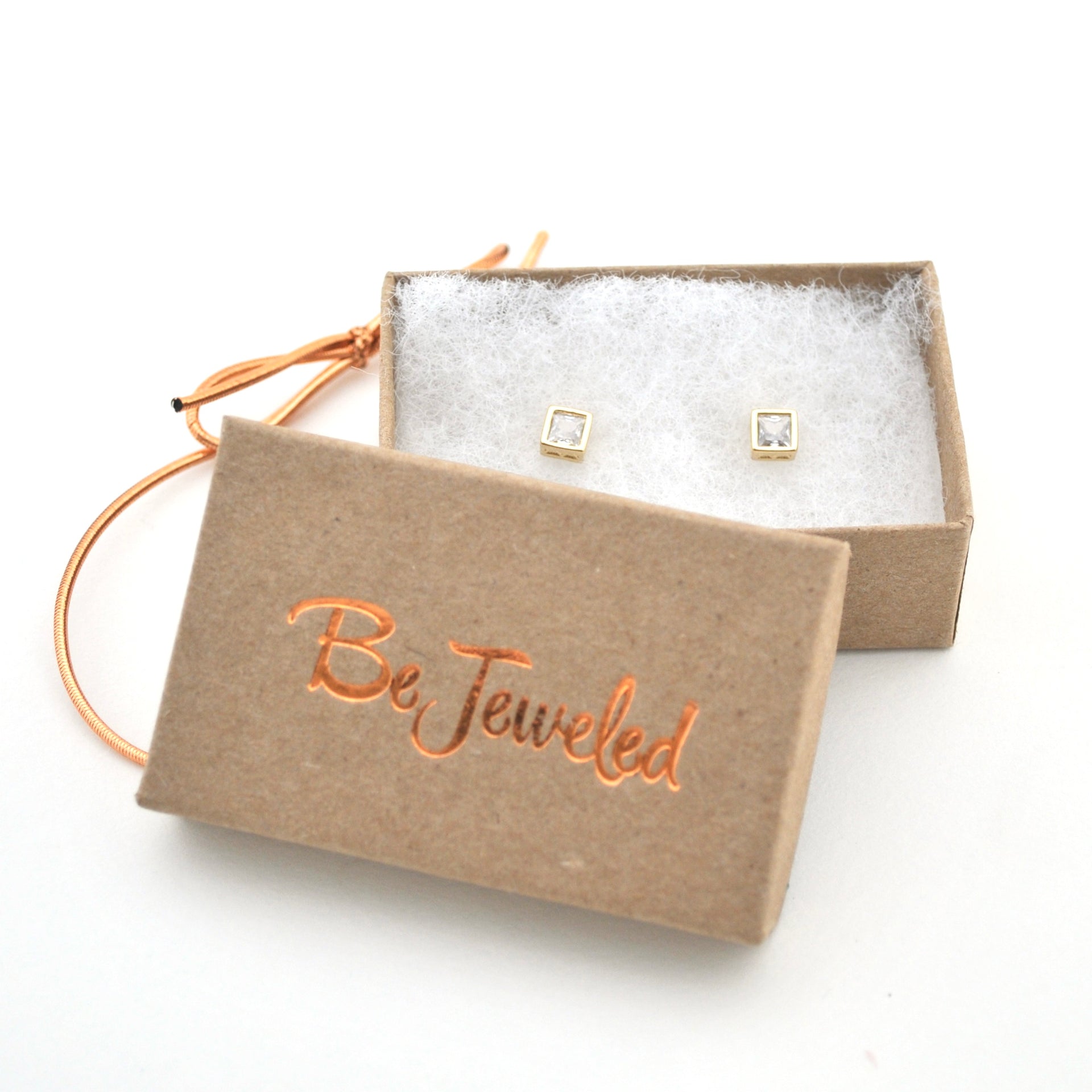 Gold square earrings in a 'Be Jeweled' box on a white background