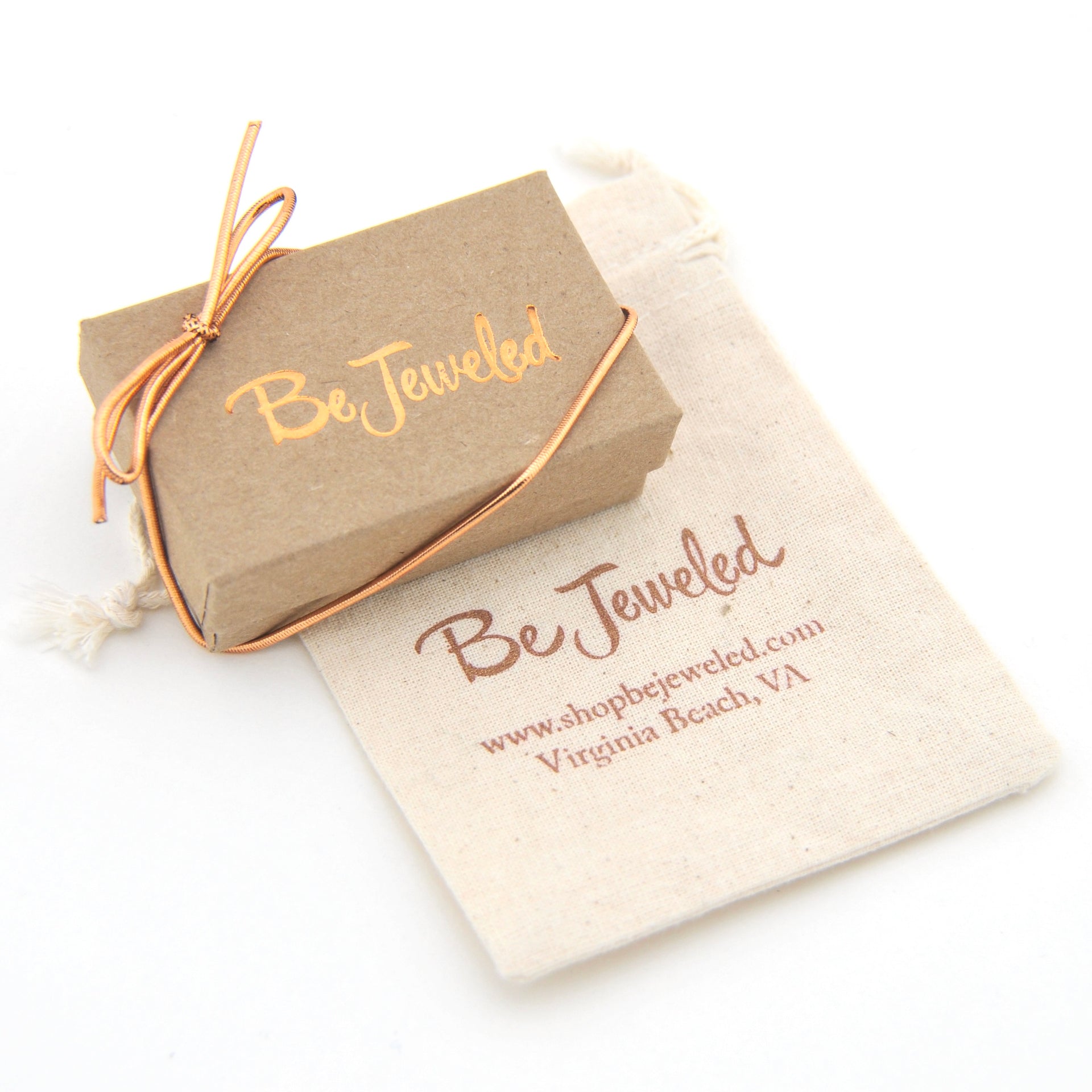 Rose gold jewelry piece on a 'Be Jeweled' branded pouch with a white background