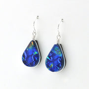 A pair of teardrop-shaped dangle earrings featuring iridescent blue and green Dichroic glass in silver bezel settings with silver fishhook wires, shown on a plain white background.