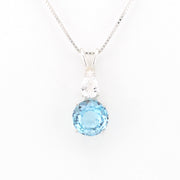 A silver pendant necklace featuring a round light blue topaz gemstone and a pear-cut clear stone, displayed on a clean white background.