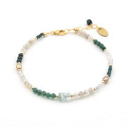 A delicate beaded bracelet featuring green, white, and light blue beads separated by small gold spacer beads, with a gold clasp and a small oval tag, shown on a plain white background.