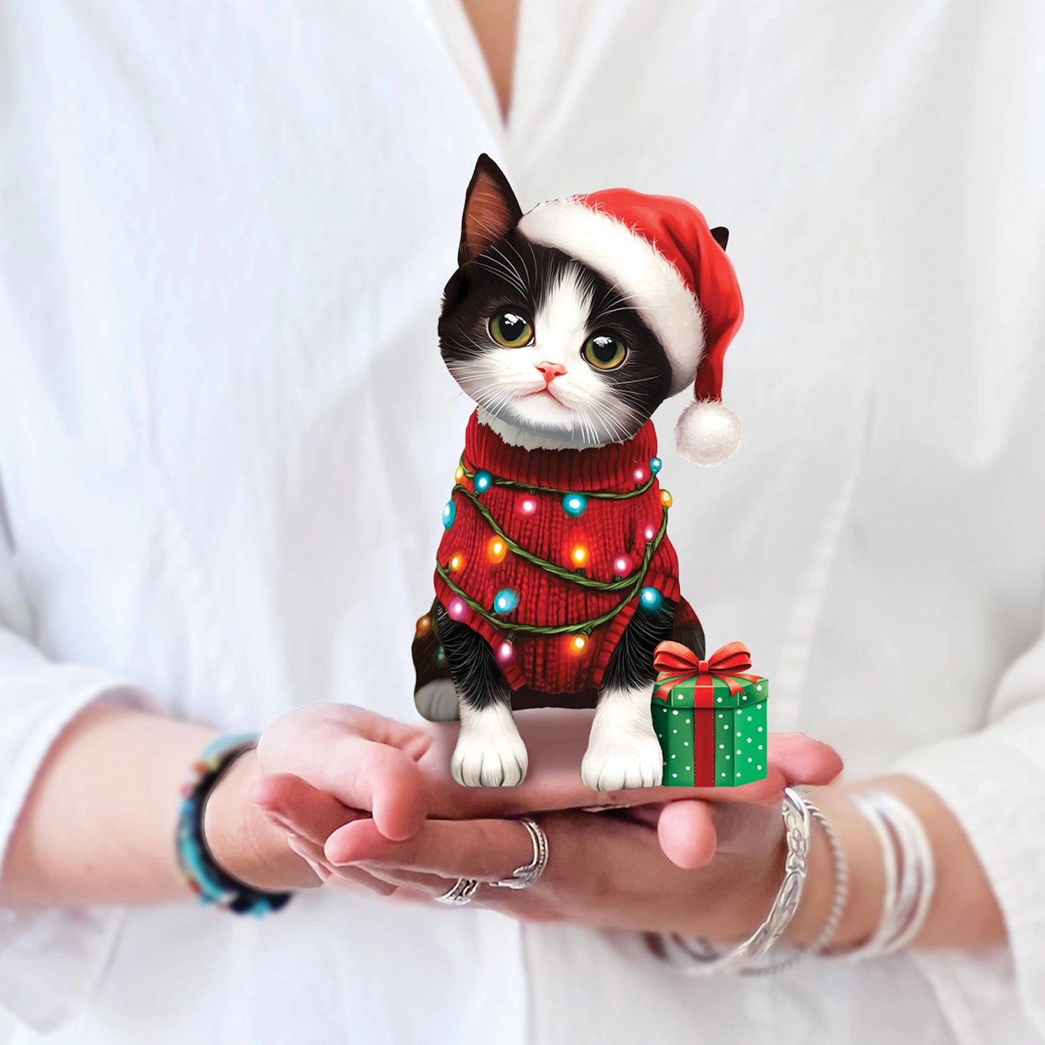 Cat figurine wearing a Santa hat and Christmas sweater held in hands against a white background
