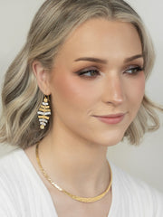 Woman wearing gold earrings and necklace against a neutral background
