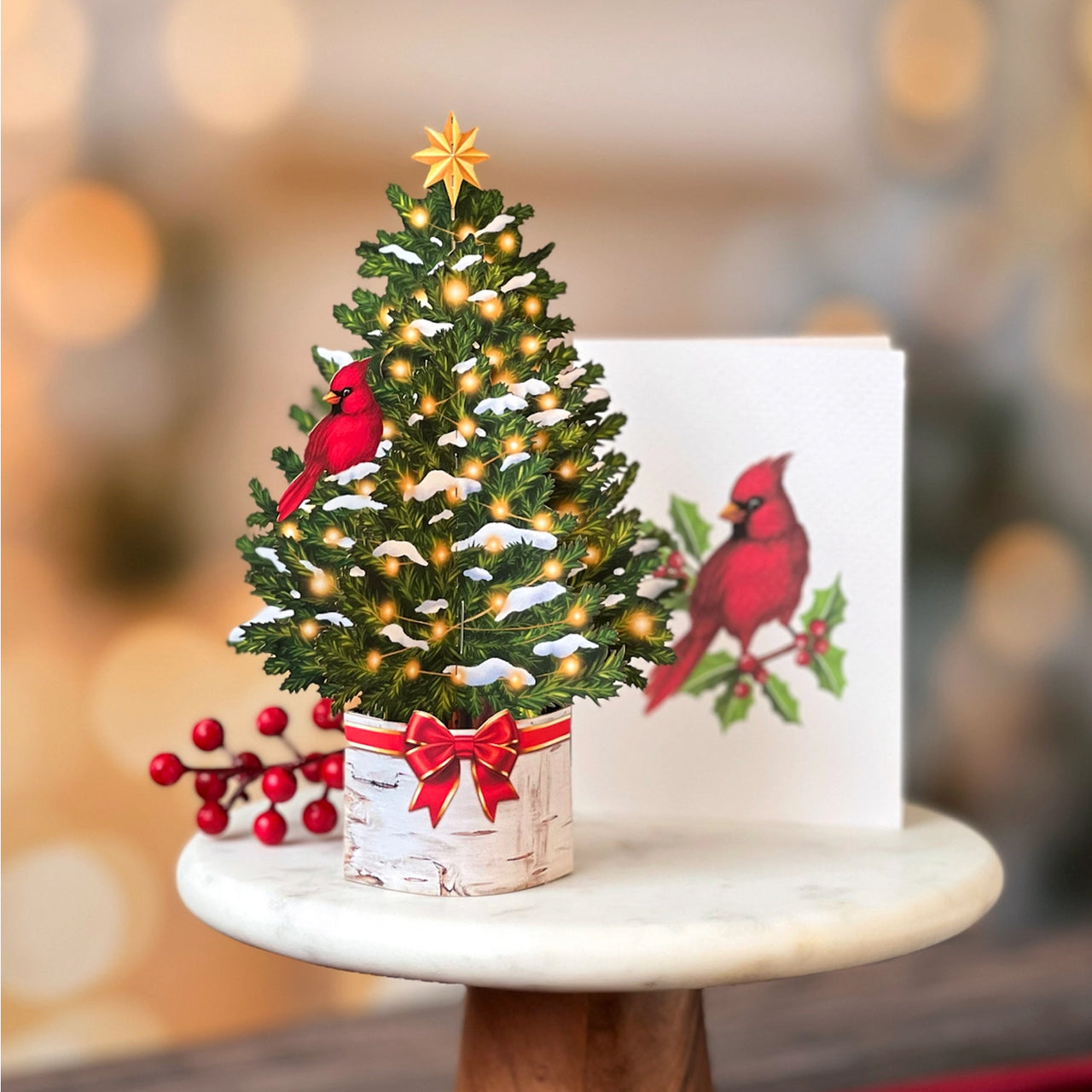 Decorative Christmas tree with lights and cardinal birds on a stand with a matching card in the background.