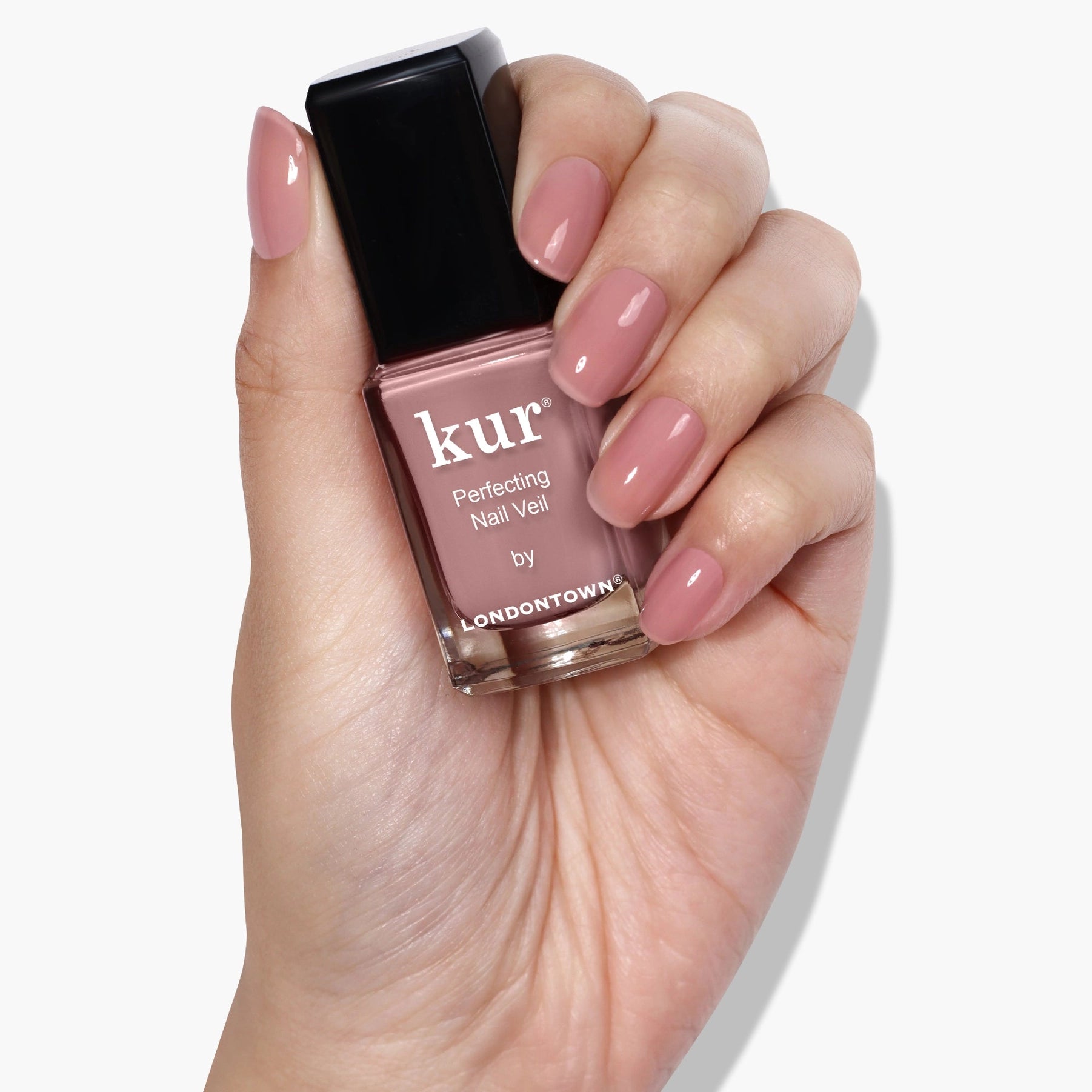 Hand holding a bottle of Londontown nail polish with matching pink nails on a white background