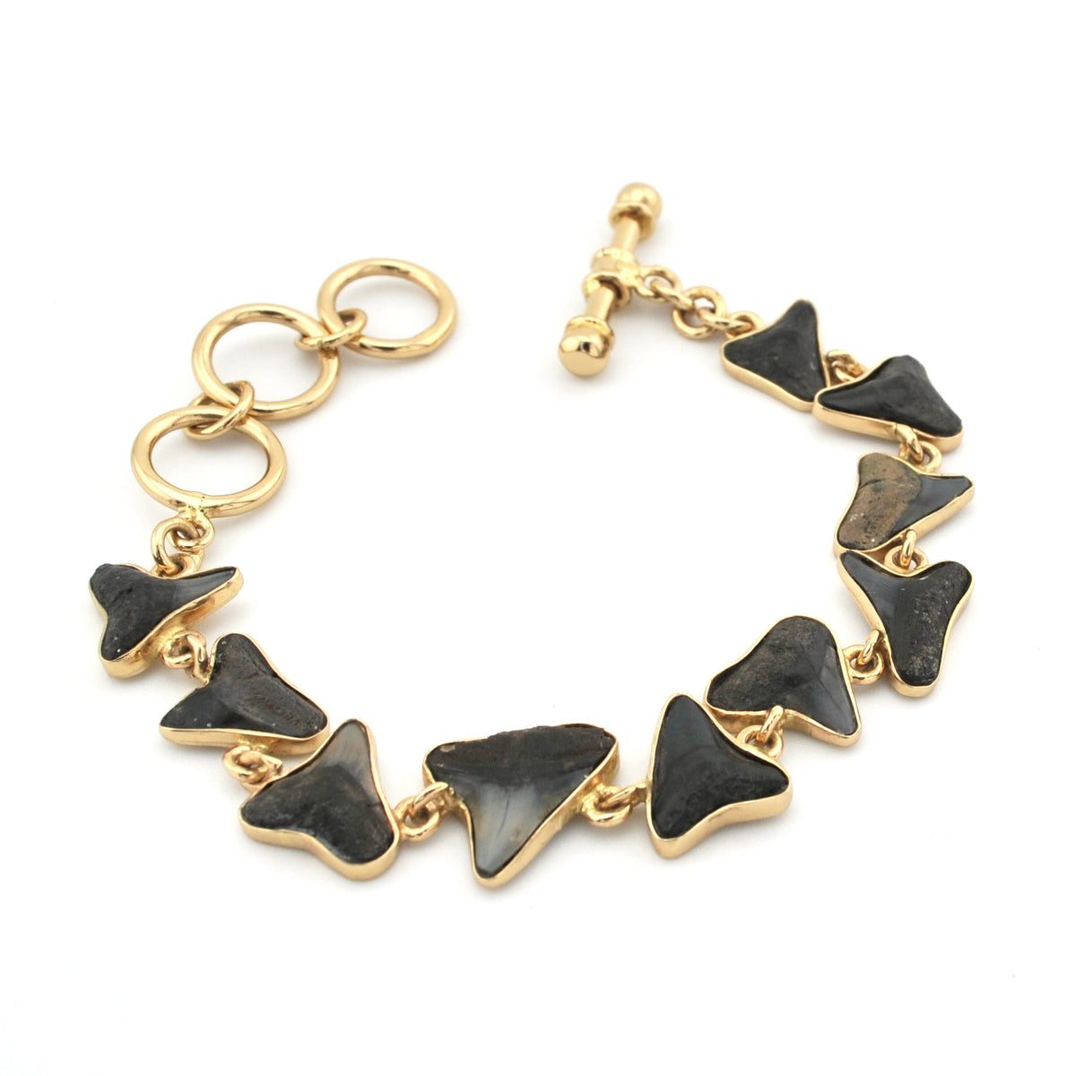 A gold-tone chain bracelet featuring multiple triangular dark gray to black shark teeth, displayed on a clean white background.