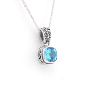 A silver pendant necklace featuring a round-cut light blue gemstone in an ornate, textured silver bezel setting, suspended from a delicate silver chain against a plain white background.