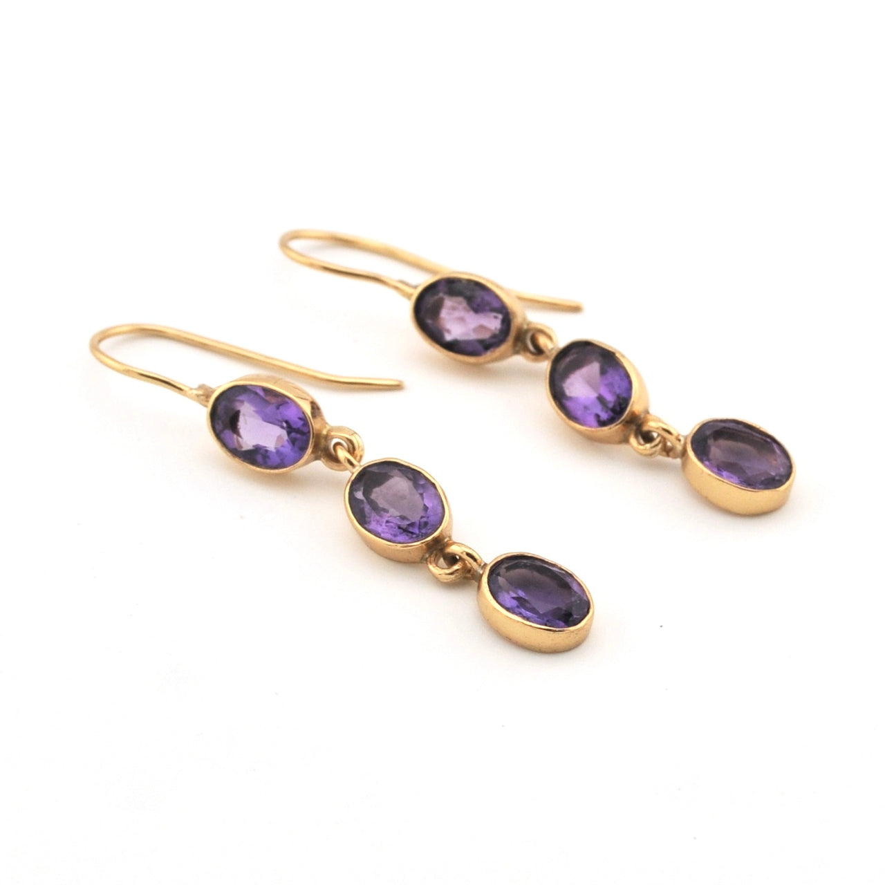 Gold earrings with purple gemstones on a white background