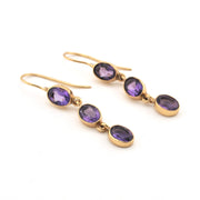 Gold earrings with purple gemstones on a white background