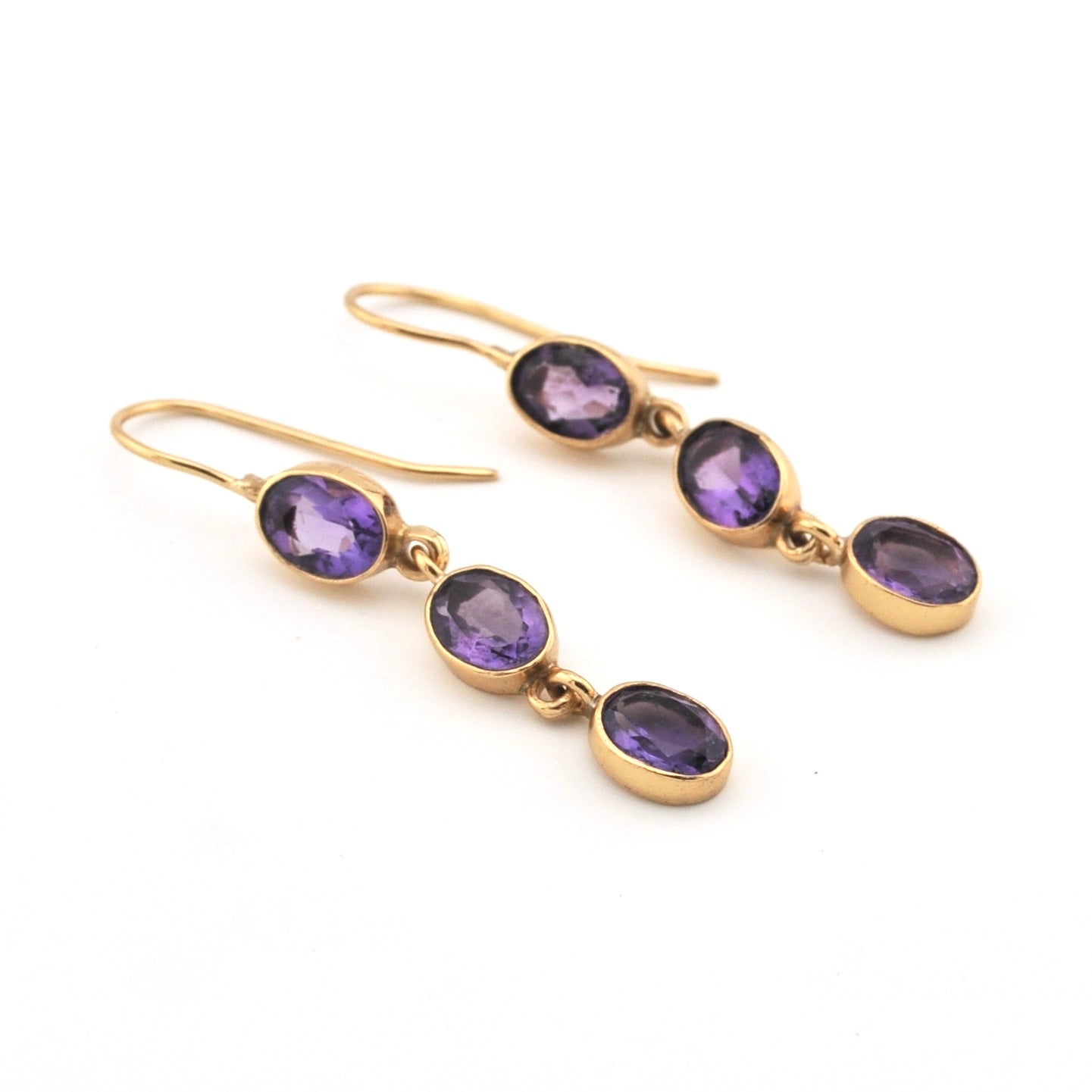 Gold earrings with purple gemstones on a white background