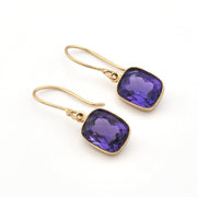 Gold earrings with purple gemstones on a white background