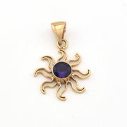 Gold sun-shaped pendant with a purple gemstone on a white background