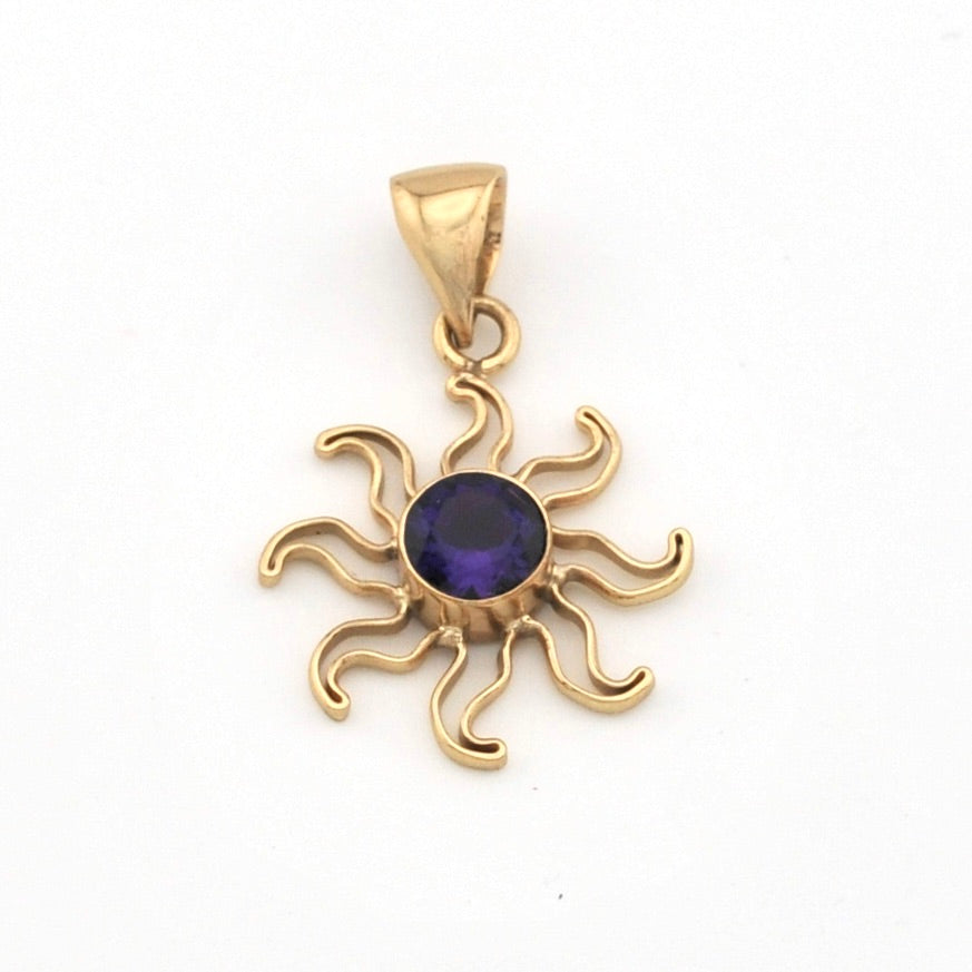 Gold sun-shaped pendant with a purple gemstone on a white background