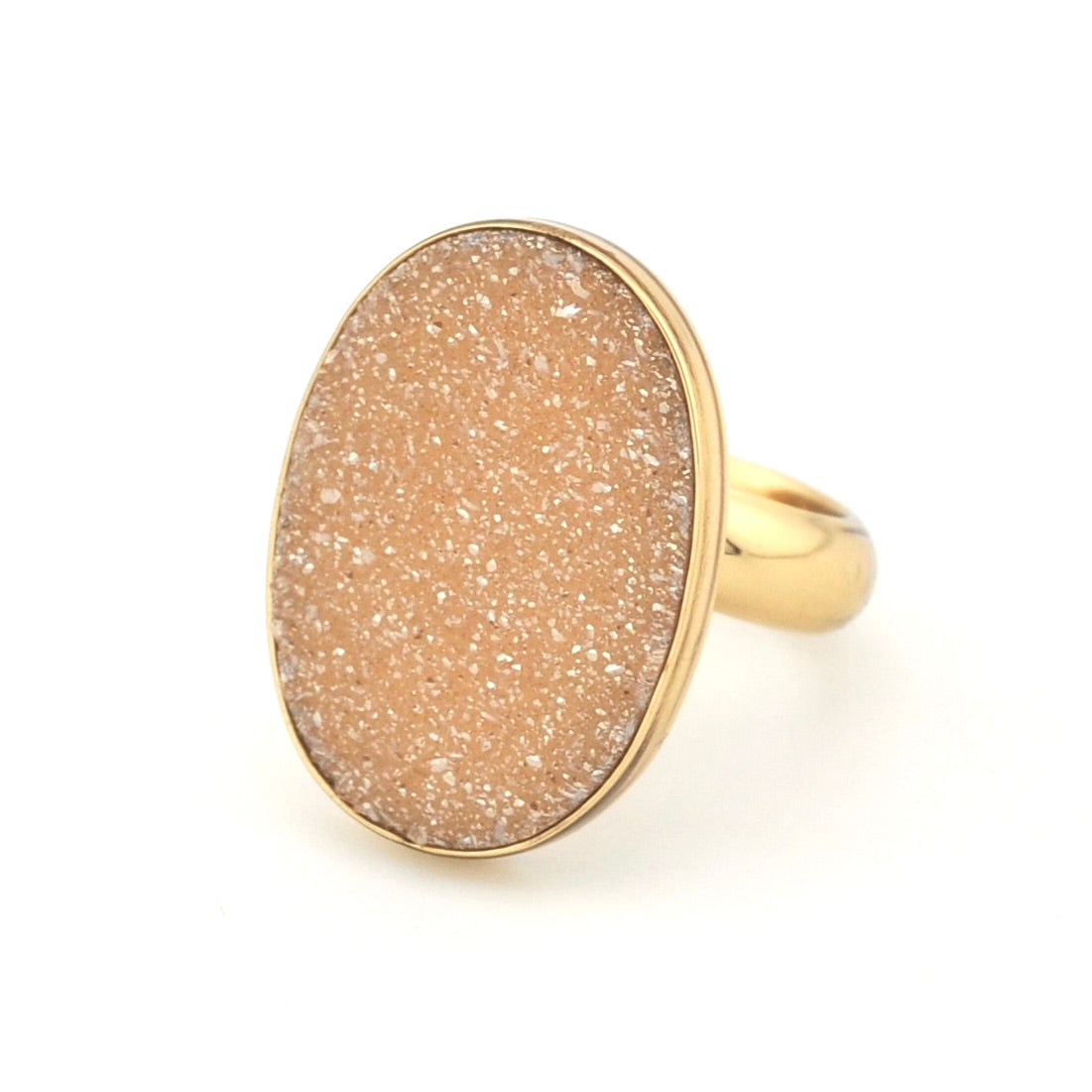 A gold ring featuring a large, oval-shaped druzy stone in a warm peach-beige color with fine white crystalline sparkle, set on a clean white background.