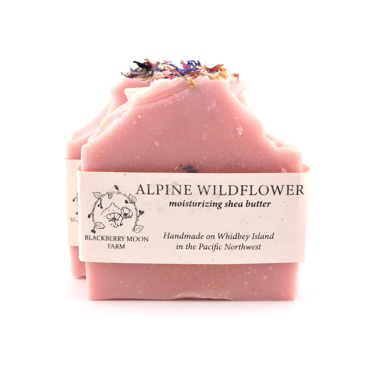 Pink soap bar with dried flowers on top and a label reading 'Alpine Wildflower' on a white background.