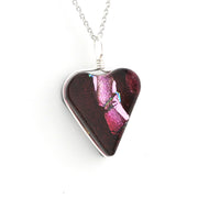 A heart-shaped glass pendant necklace with a dark red and pink iridescent pattern, set in a silver-tone metal frame and suspended from a silver chain against a white background.