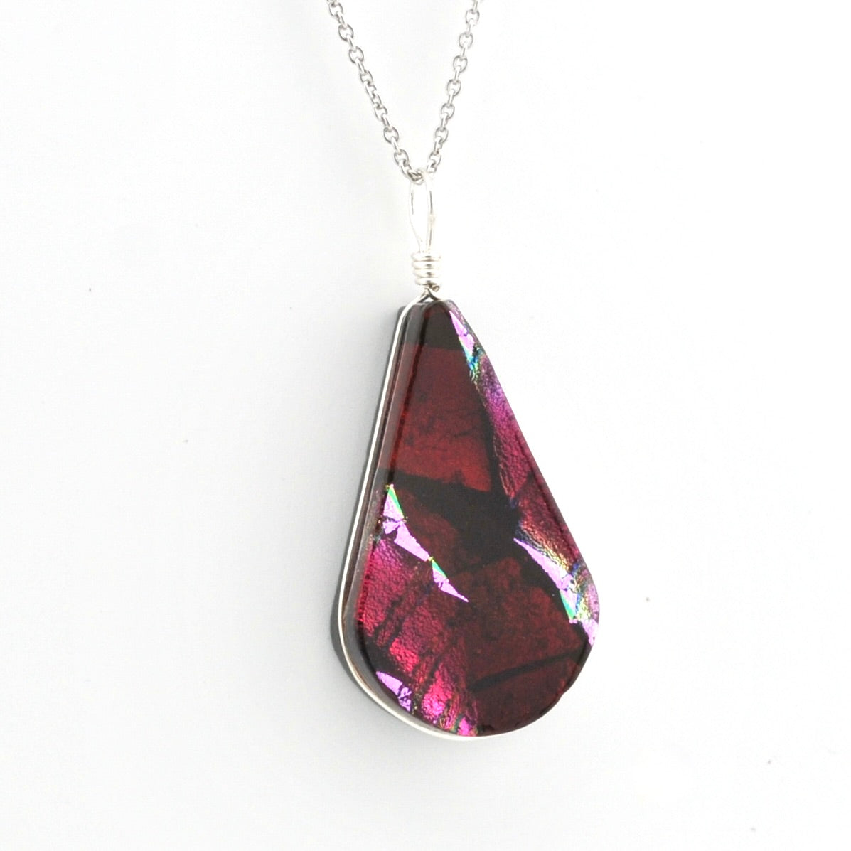 A teardrop-shaped pendant necklace featuring a dark red and magenta iridescent dichroic glass with silver metal borders and a silver chain, shown against a plain white background.