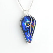 A silver wire-wrapped pendant necklace featuring a vibrant blue iridescent dichroic glass with rainbow reflections, suspended from a delicate silver chain against a plain white background.
